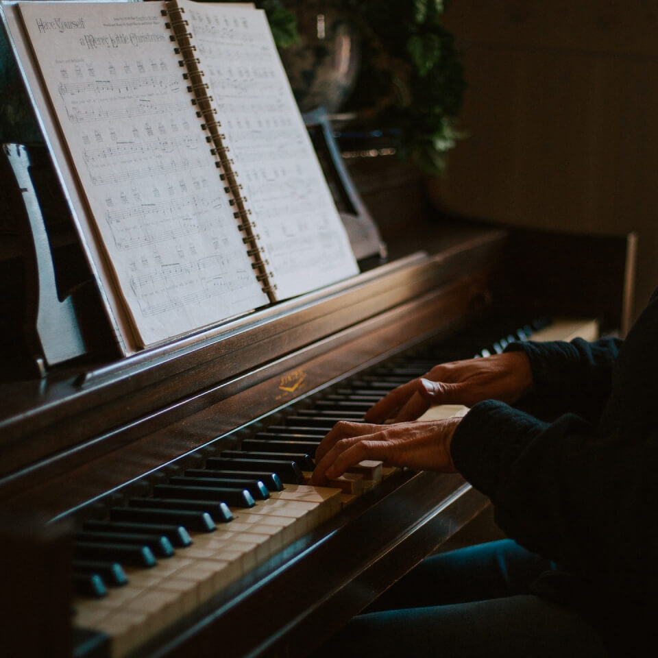 Hände auf den Tasten eines Klaviers mit aufgeschlagenen Noten